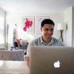 man in gray hoodie sitting on chair in front of silver macbook